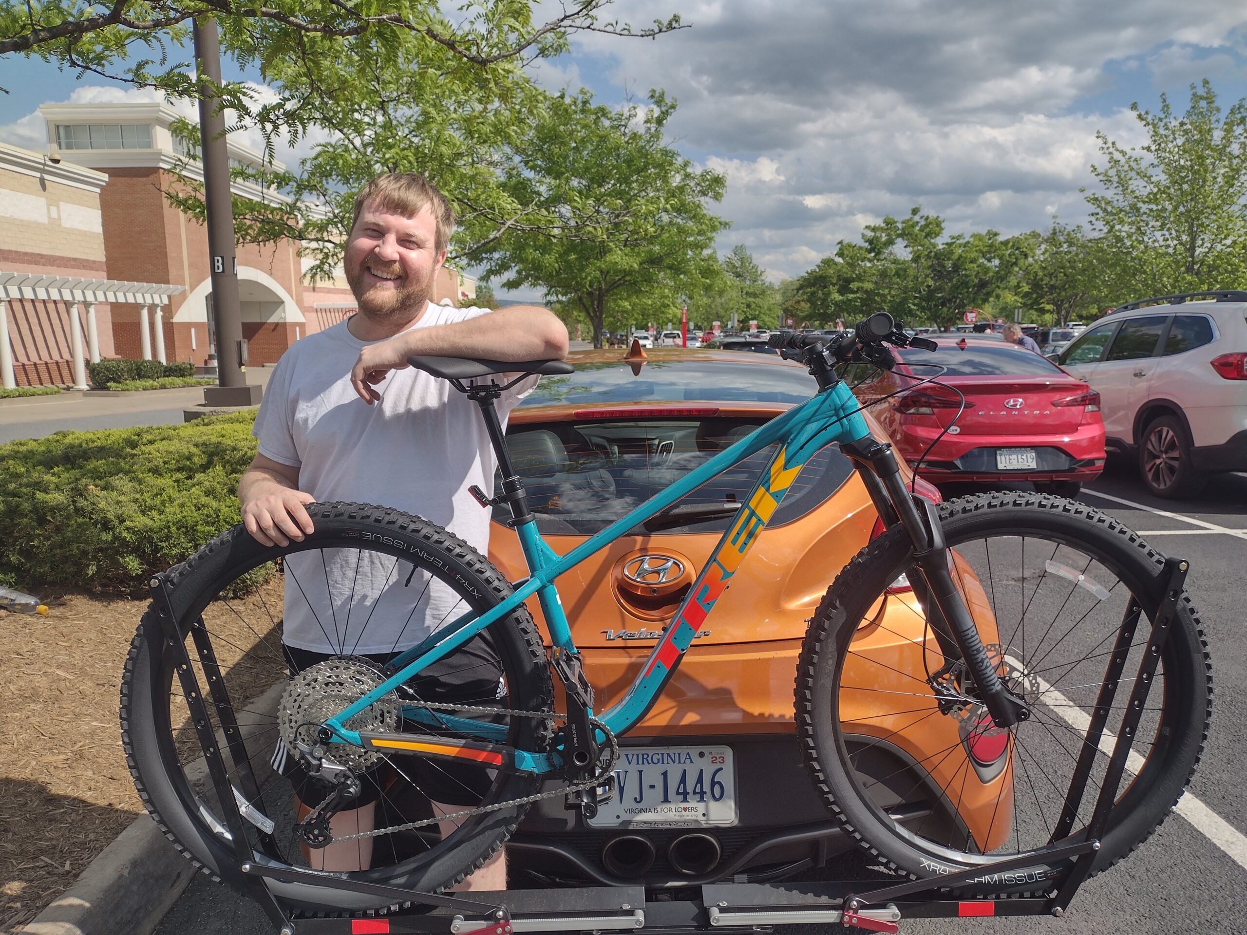 A photograph of Daniel Lee Mills with his Trek Roscoe Mountain Bike and Veloster Turbo. Taken in April 2023.